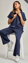 Woman wearing a navy blue outfit sitting on a white stool against a plain background