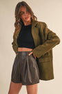 Woman wearing an olive green coat and black leather shorts on a beige background