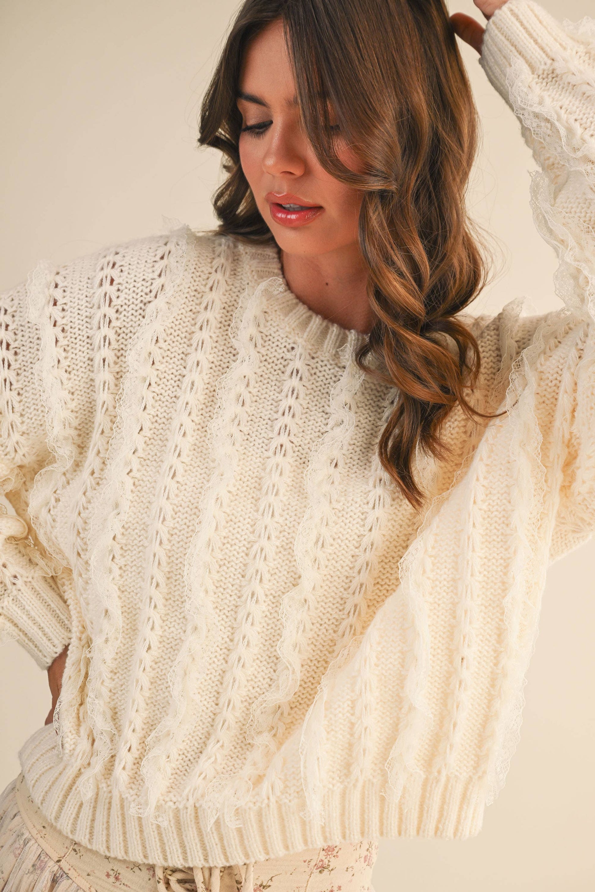 Woman wearing a cream-colored knitted sweater against a neutral background