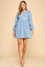 Woman wearing a blue dress with long sleeves and lace-up front on a beige background