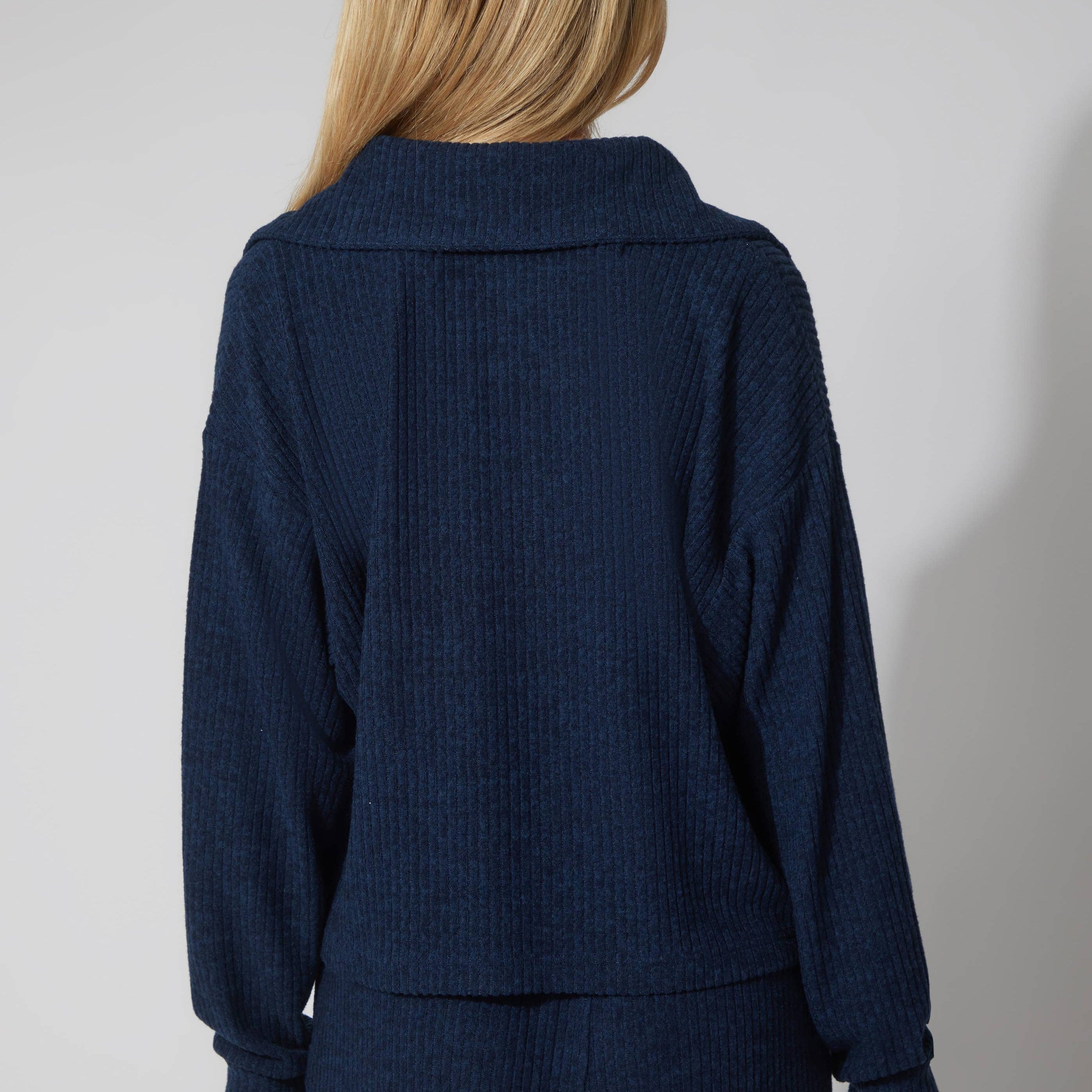Person wearing a navy blue ribbed sweater and pants on a plain background