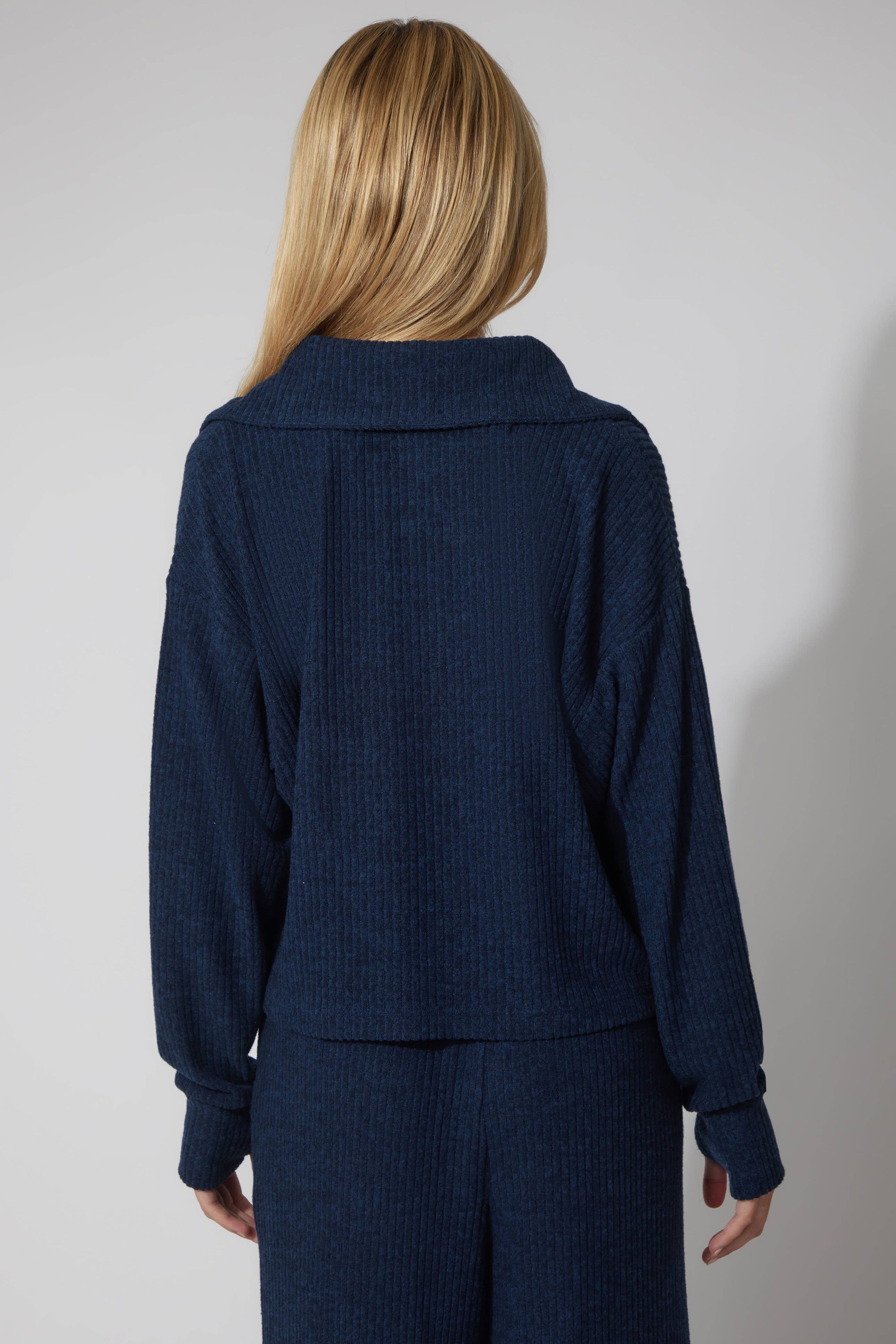 Person wearing a navy blue ribbed sweater and pants on a plain background
