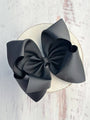 Two black hair bows on a white circular base against a light wooden background