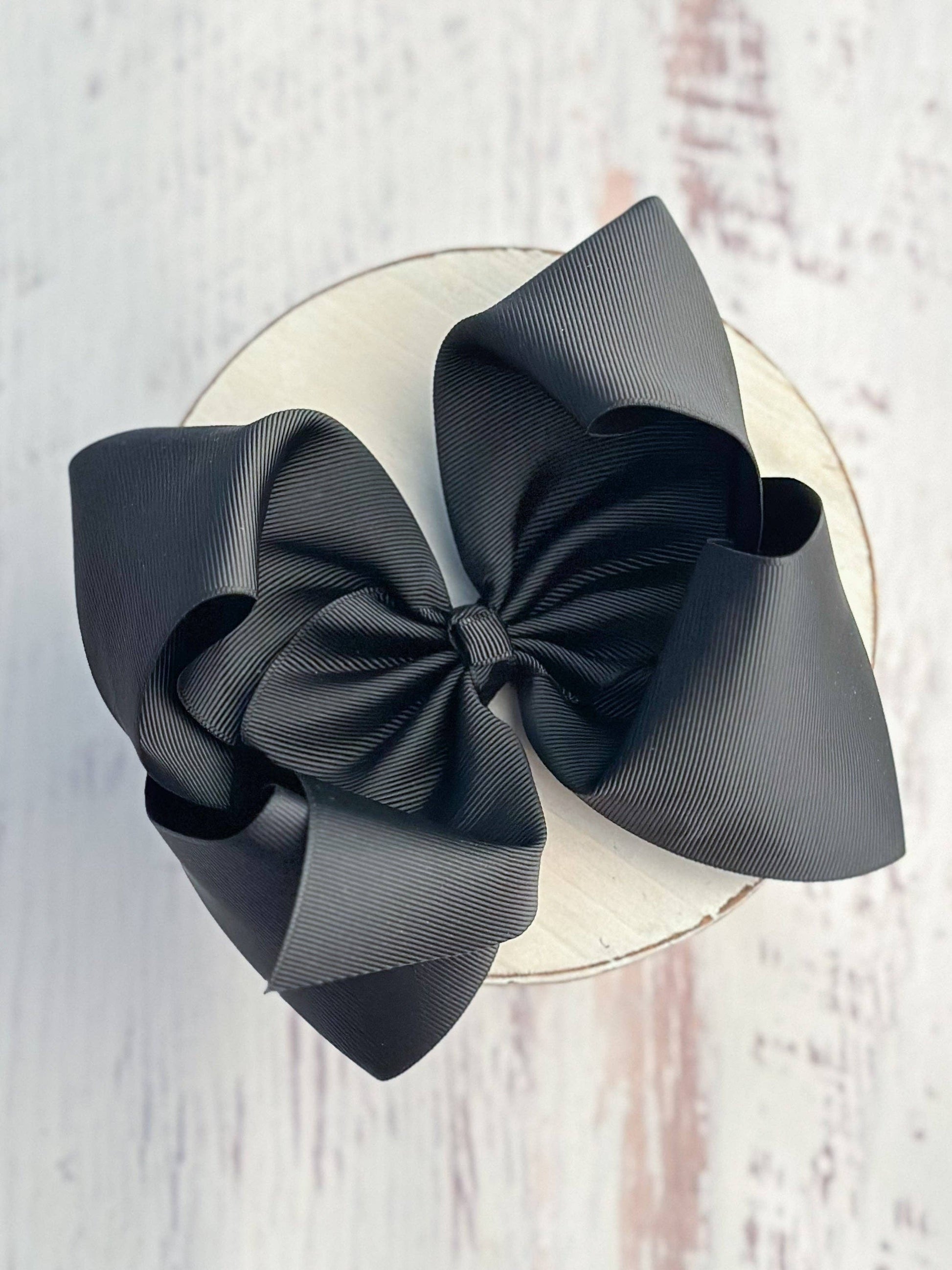 Two black hair bows on a white circular base against a light wooden background