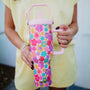 Person holding a colorful floral-patterned tumbler with a pink handle.
