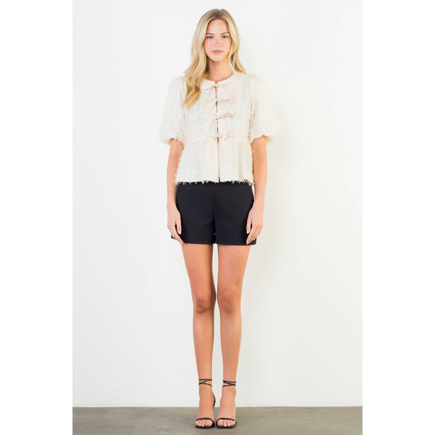Woman wearing a white blouse and black shorts on a plain background
