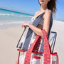 Woman on a beach holding a red and white checkered bag with a blue sky and ocean in the background