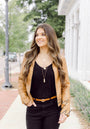 Woman wearing a tan jacket and black outfit with a necklace, standing outdoors.
