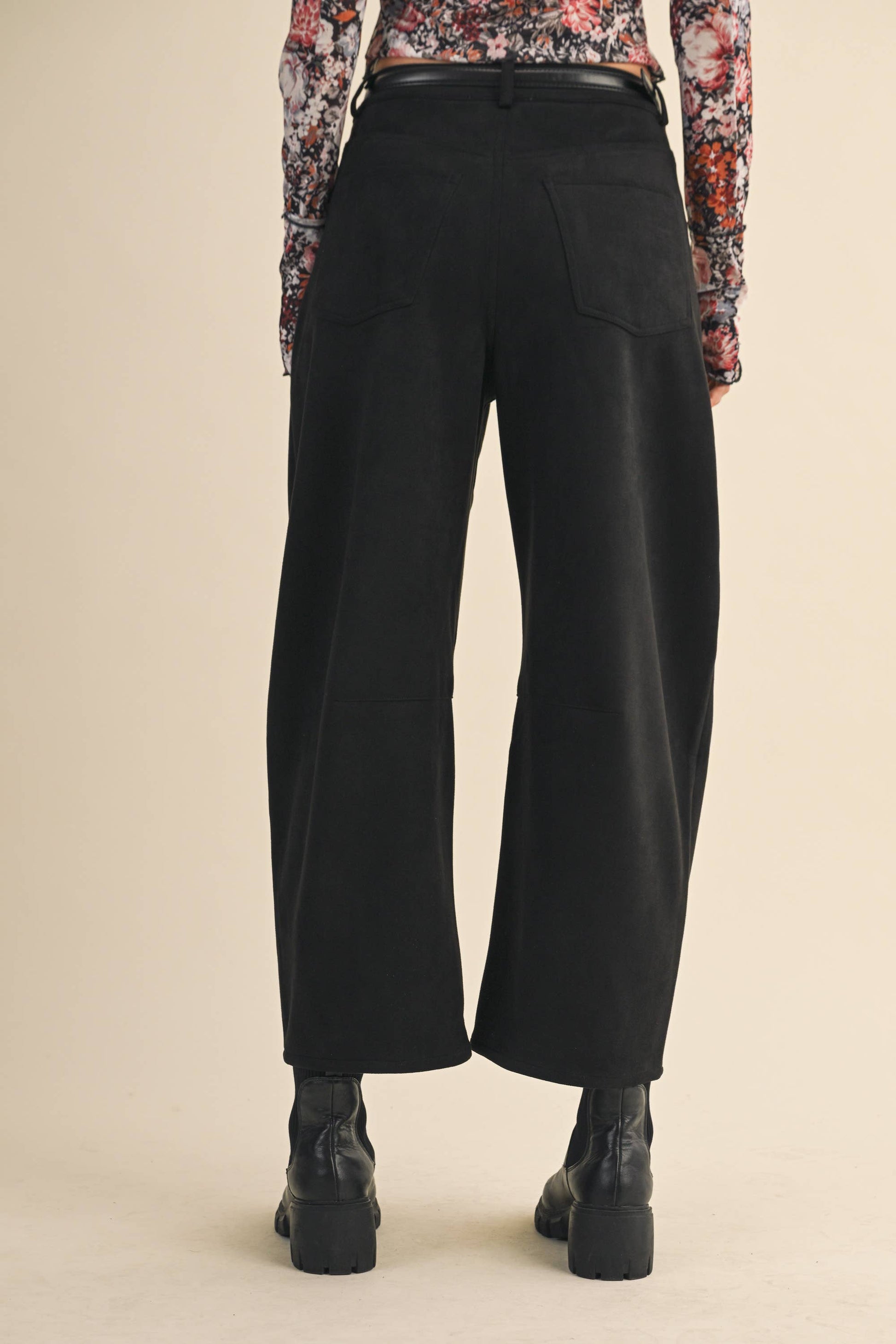 Black wide-leg pants worn with a floral top on a beige background