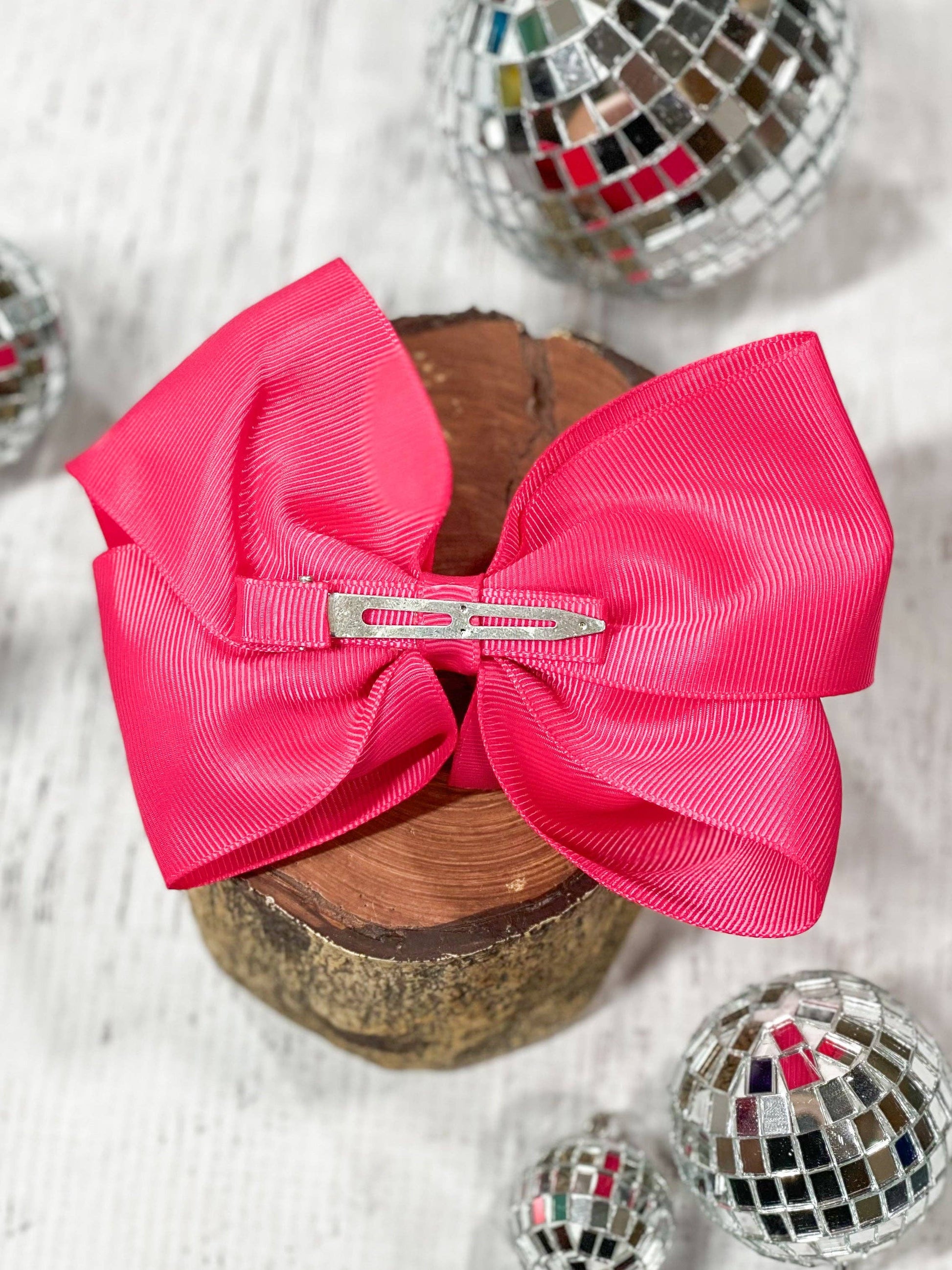 Large pink bow with a clip on a wooden block with disco balls in the background