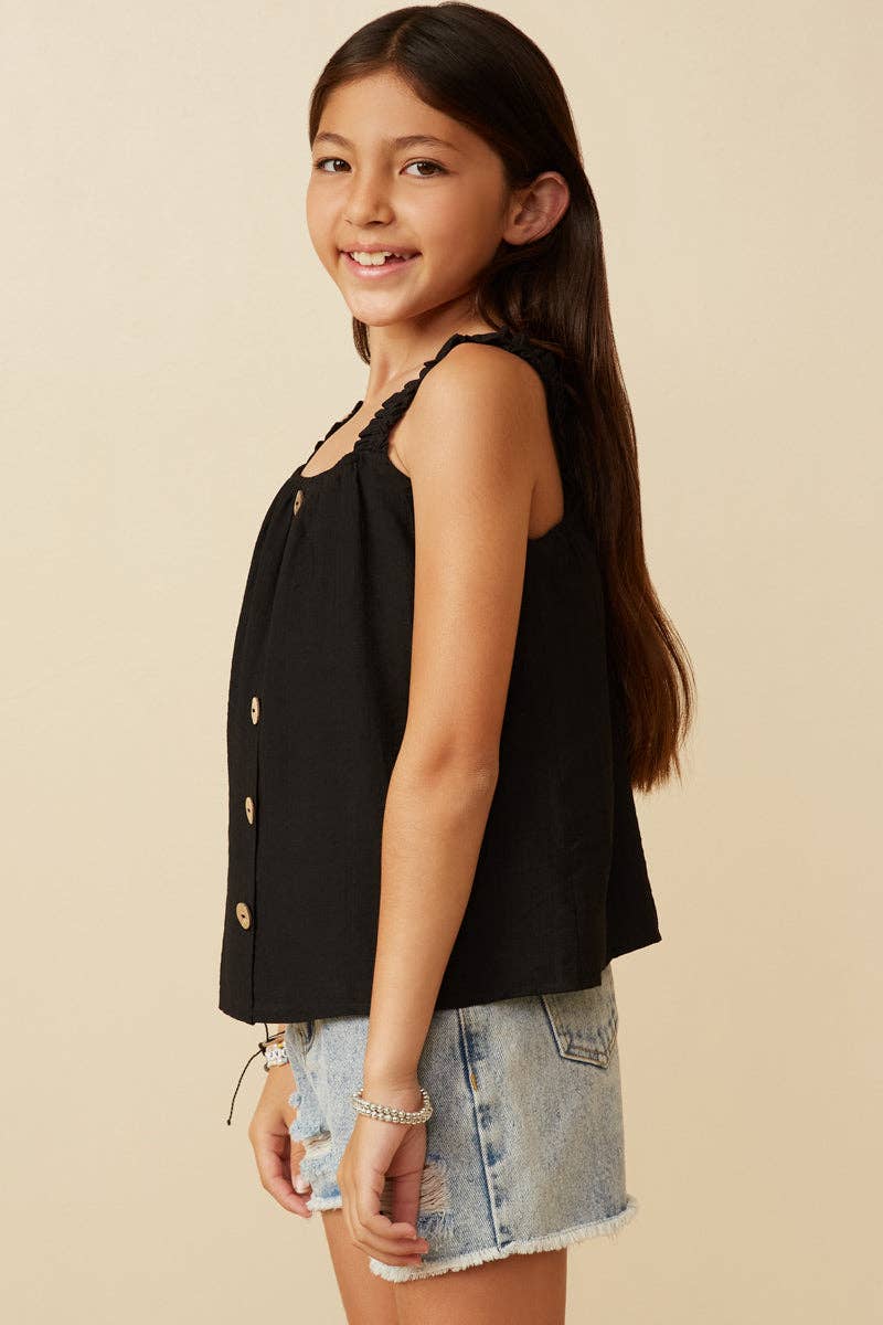 Young girl wearing a black sleeveless top and denim shorts on a beige background