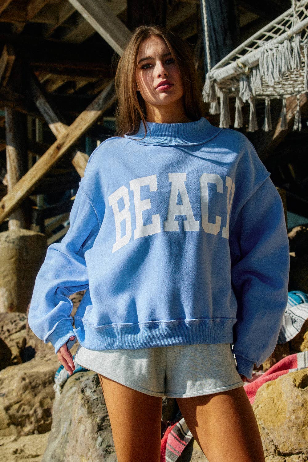 Person wearing a blue sweatshirt with 'BEACH' text in a rustic outdoor setting