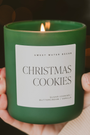 Green candle labeled 'Christmas Cookies' held by a hand with a blurred background