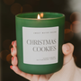 Green candle labeled 'Christmas Cookies' held by a hand with a blurred background
