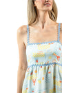 Woman wearing a light blue dress with floral pattern and lace trim on a white background