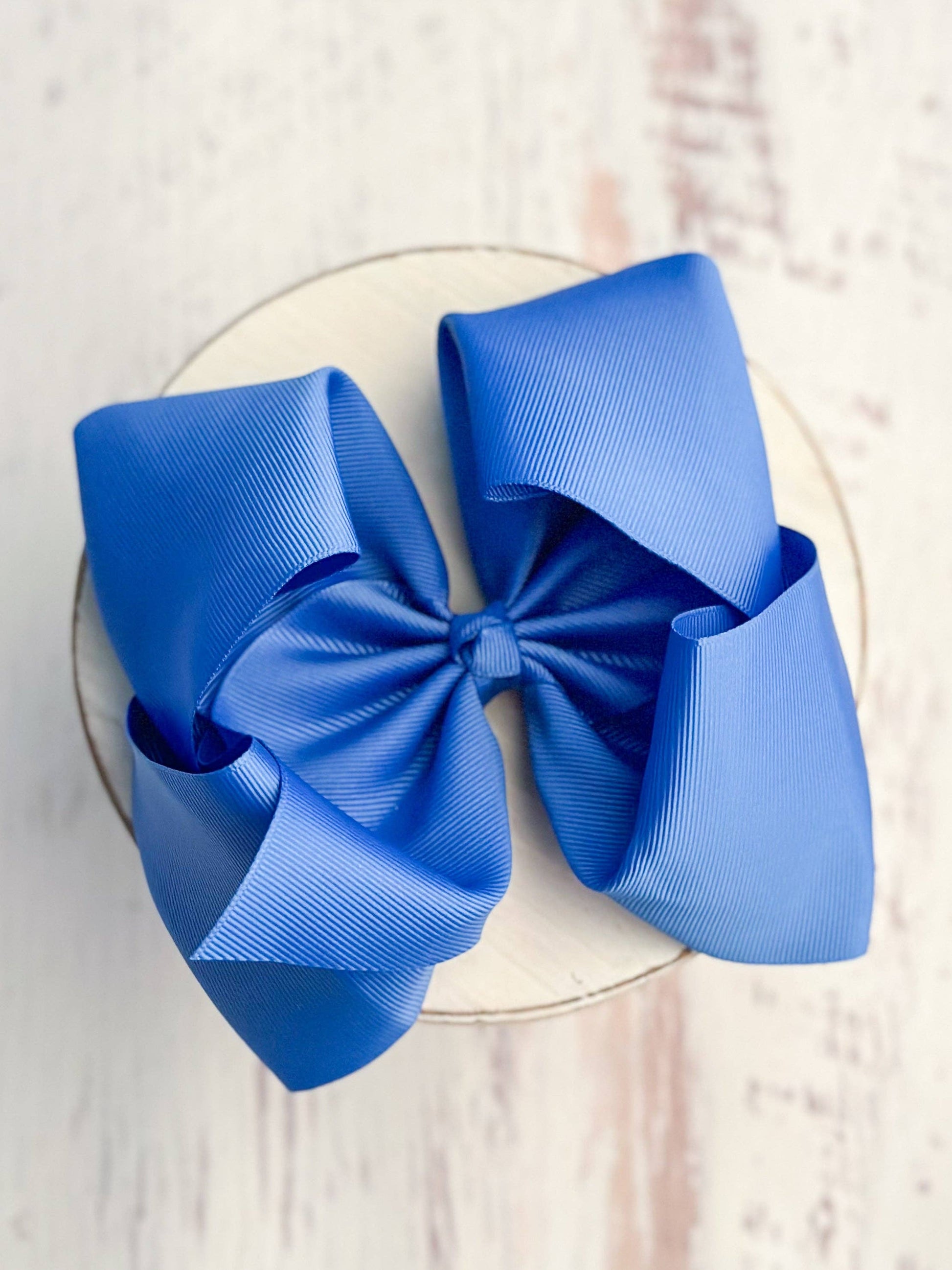 Blue hair bow on a white plate with a light wooden background
