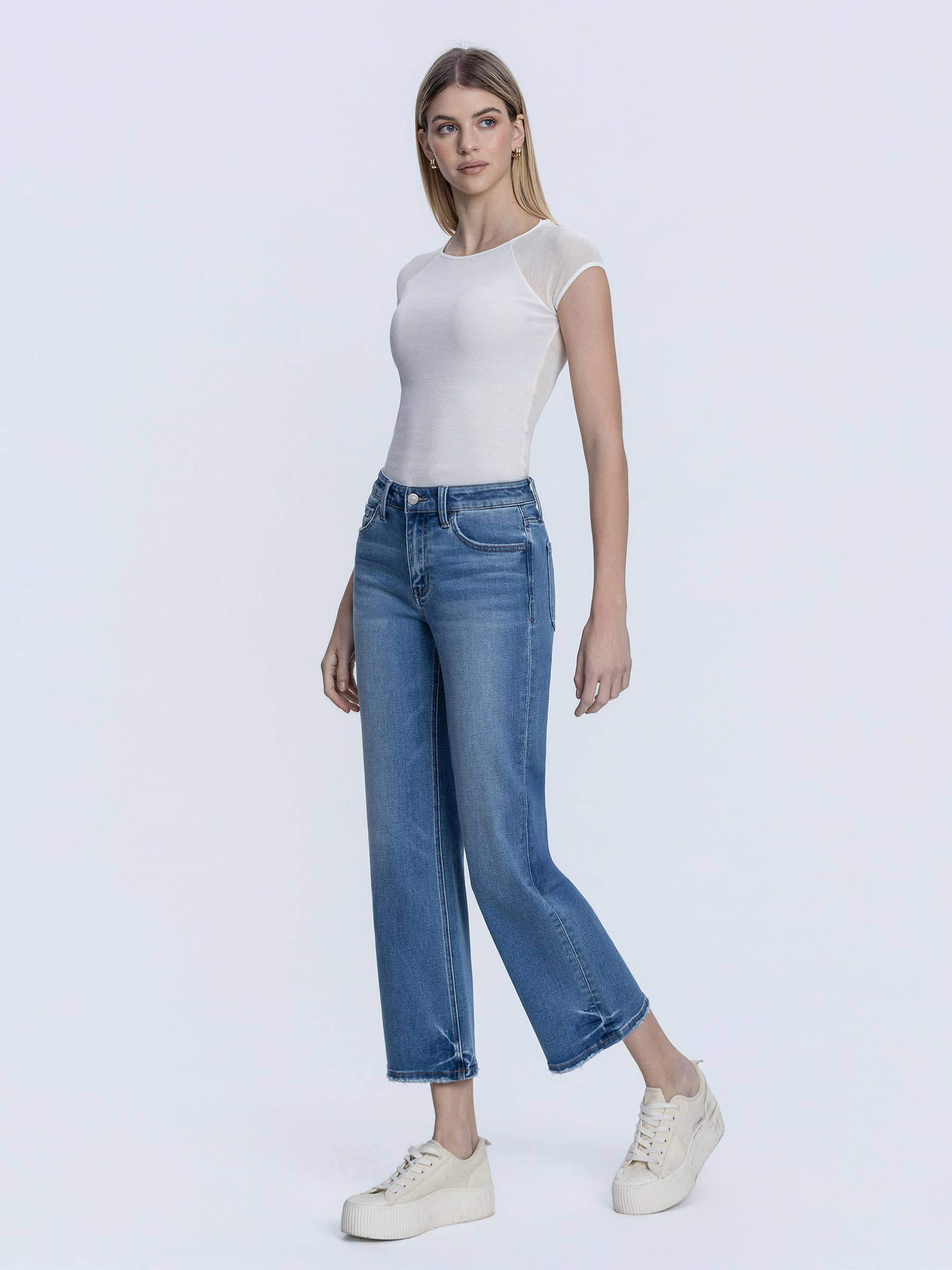 Woman wearing a white top and blue jeans on a light gray background