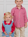 Two children, a girl in a blue dress with red collar and a boy in a red and white checkered shirt and beige pants, standing against a white background.