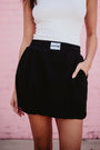 Person wearing a black skirt with a visible brand label against a pink background