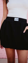 Person wearing a black skirt with a visible brand label against a pink background