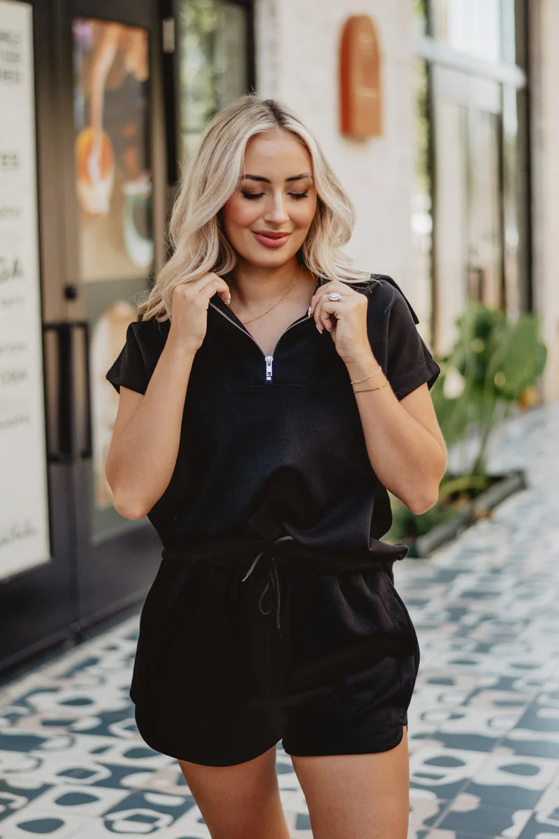 Woman wearing a black outfit standing on a patterned floor.