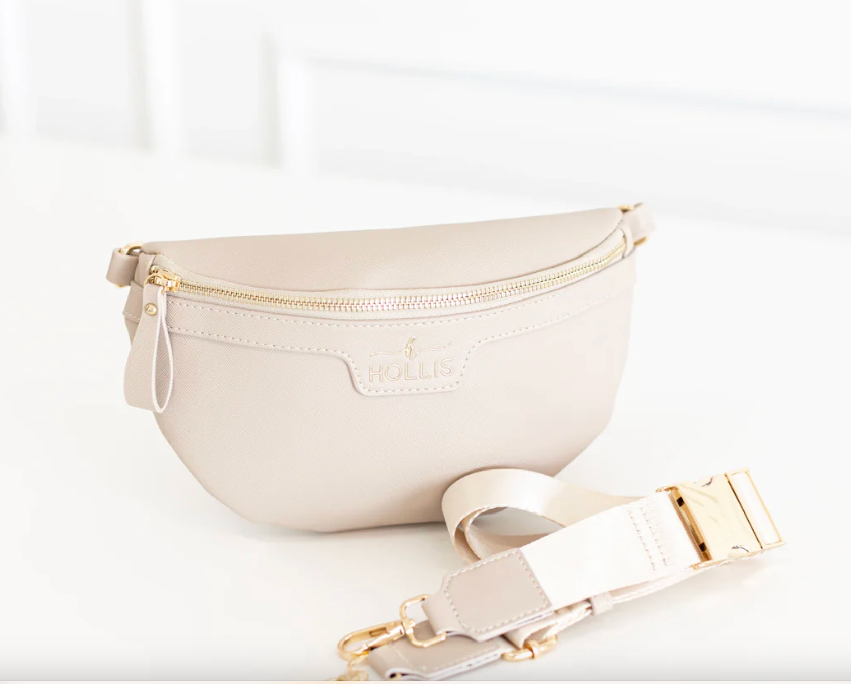 Beige fanny pack with gold zipper and strap on a white background