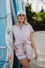 Woman in a light pink outfit standing next to a surfboard with 'YOLOBOARD' branding.