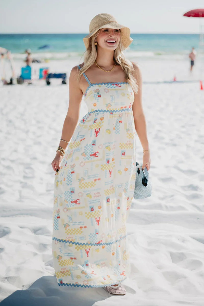 Woman in a long, patterned dress standing on a sandy beach.