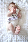 Baby lying on bedding with pacifier and linen clip attached to clothing