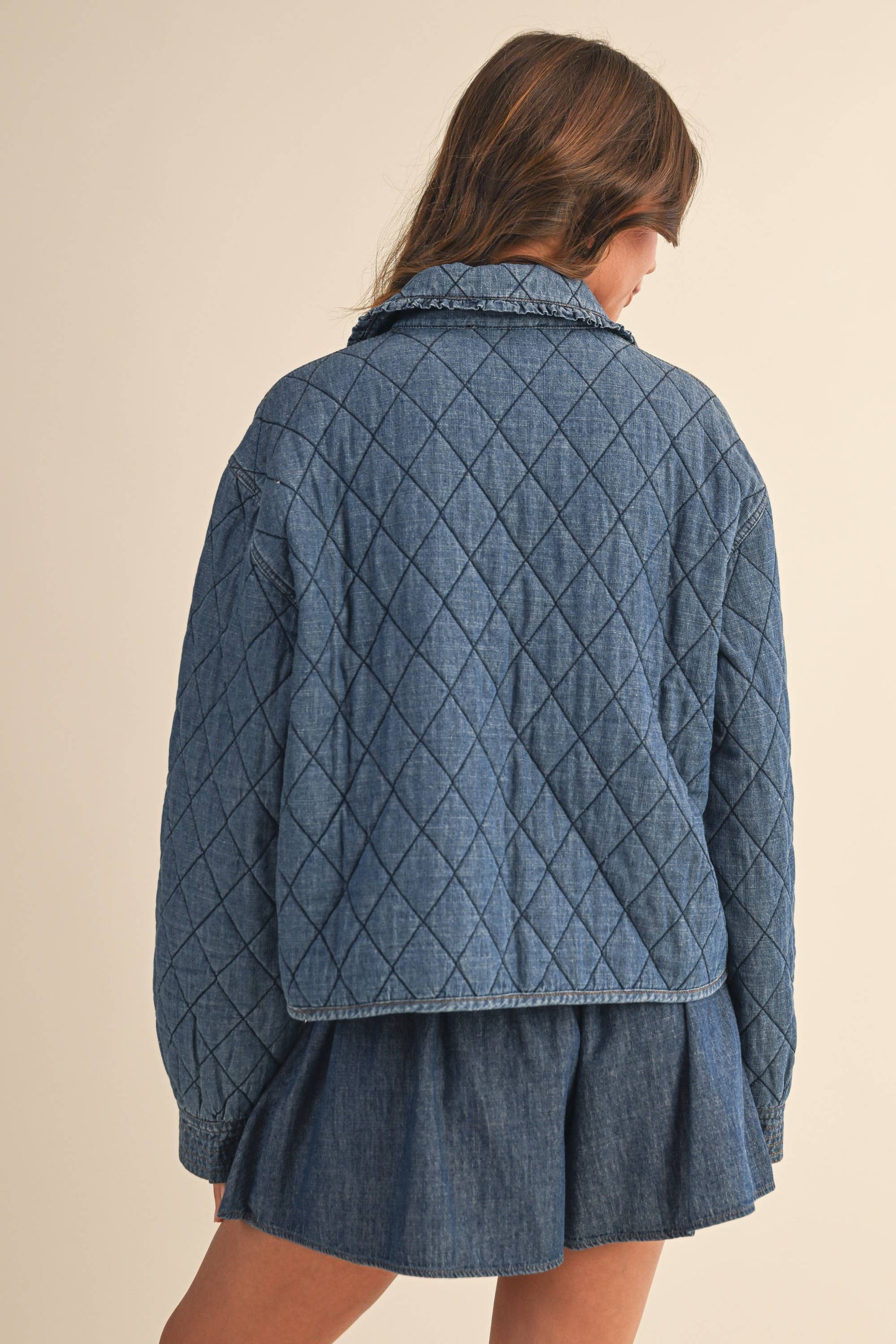 Woman wearing a blue quilted jacket with a skirt against a beige background