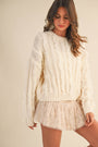 Woman wearing a cream-colored knit sweater and skirt set against a plain background