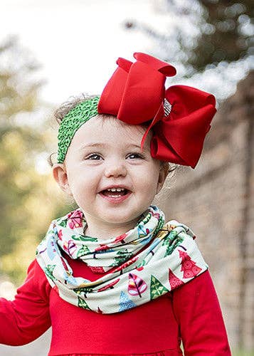 Child wearing a red bow headband and a colorful scarf outdoors