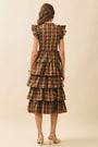 Woman wearing a brown plaid dress with ruffled sleeves on a beige background
