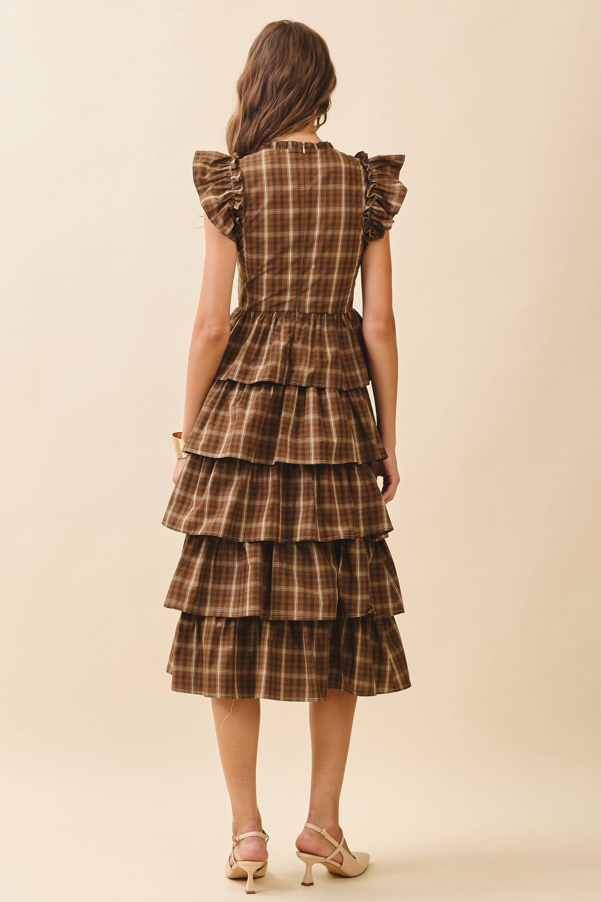 Woman wearing a brown plaid dress with ruffled sleeves on a beige background