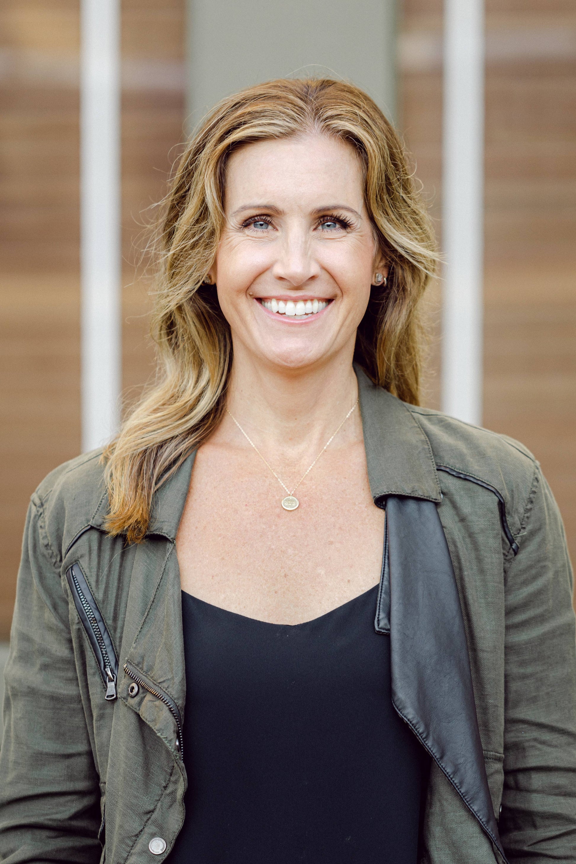 Woman wearing a green jacket and black top with a neutral background