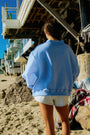 Person wearing a blue jacket and shorts on a beach with a lifeguard tower in the background.