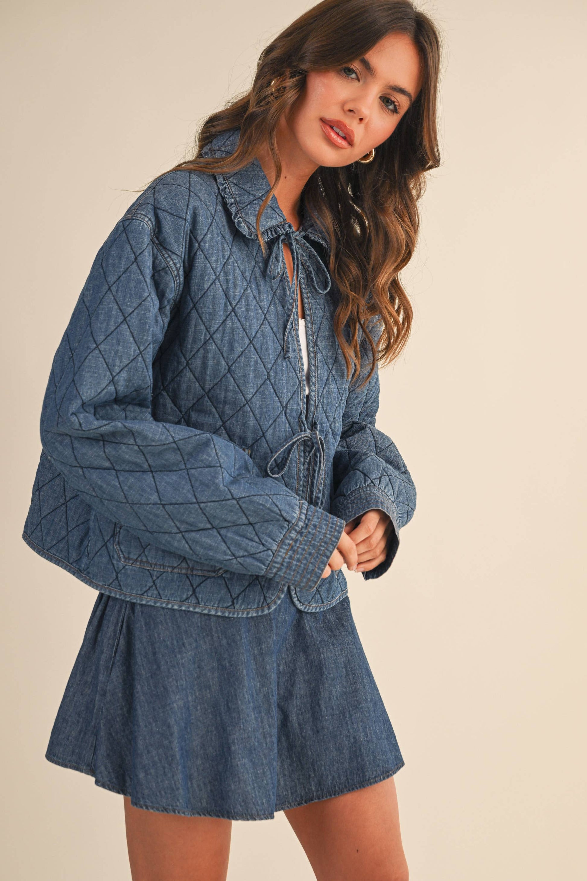 Woman wearing a blue quilted jacket with a skirt against a beige background