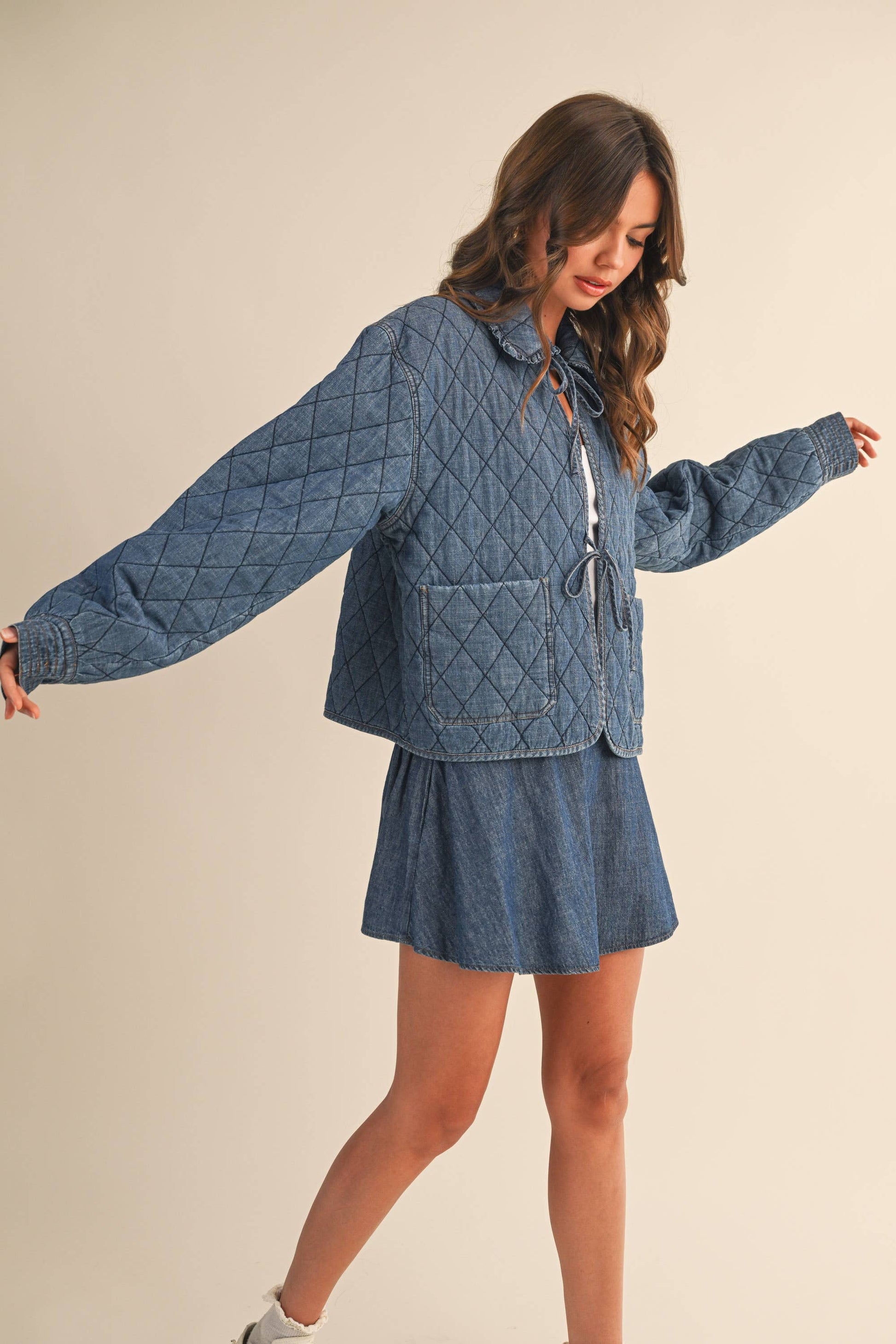 Woman wearing a blue quilted jacket with a skirt against a beige background