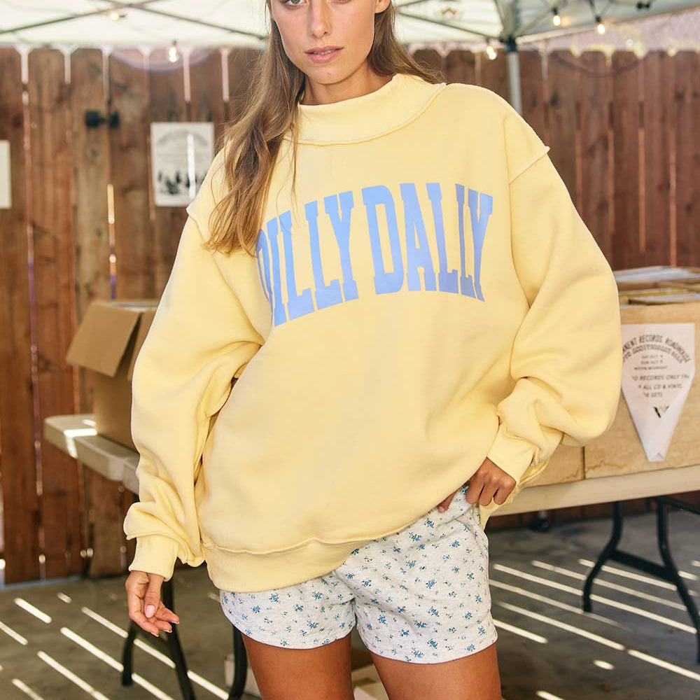 Woman wearing a yellow sweatshirt with 'Hilly Daily' text in an outdoor setting.