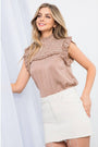 Woman wearing a patterned top and white skirt on a plain background