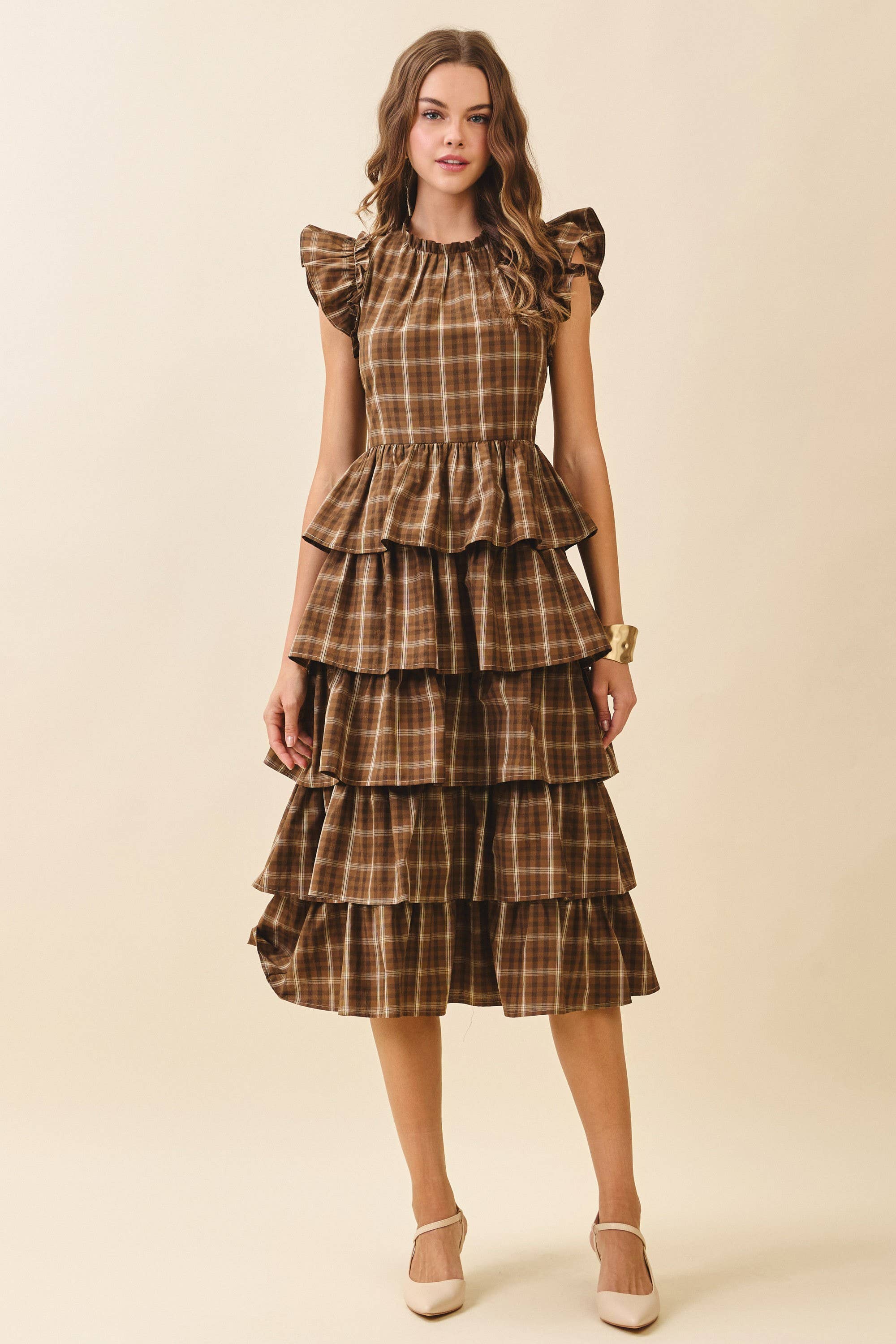 Woman wearing a plaid dress with ruffled layers on a beige background