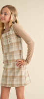 Young girl wearing a plaid dress over a long-sleeve shirt against a beige background