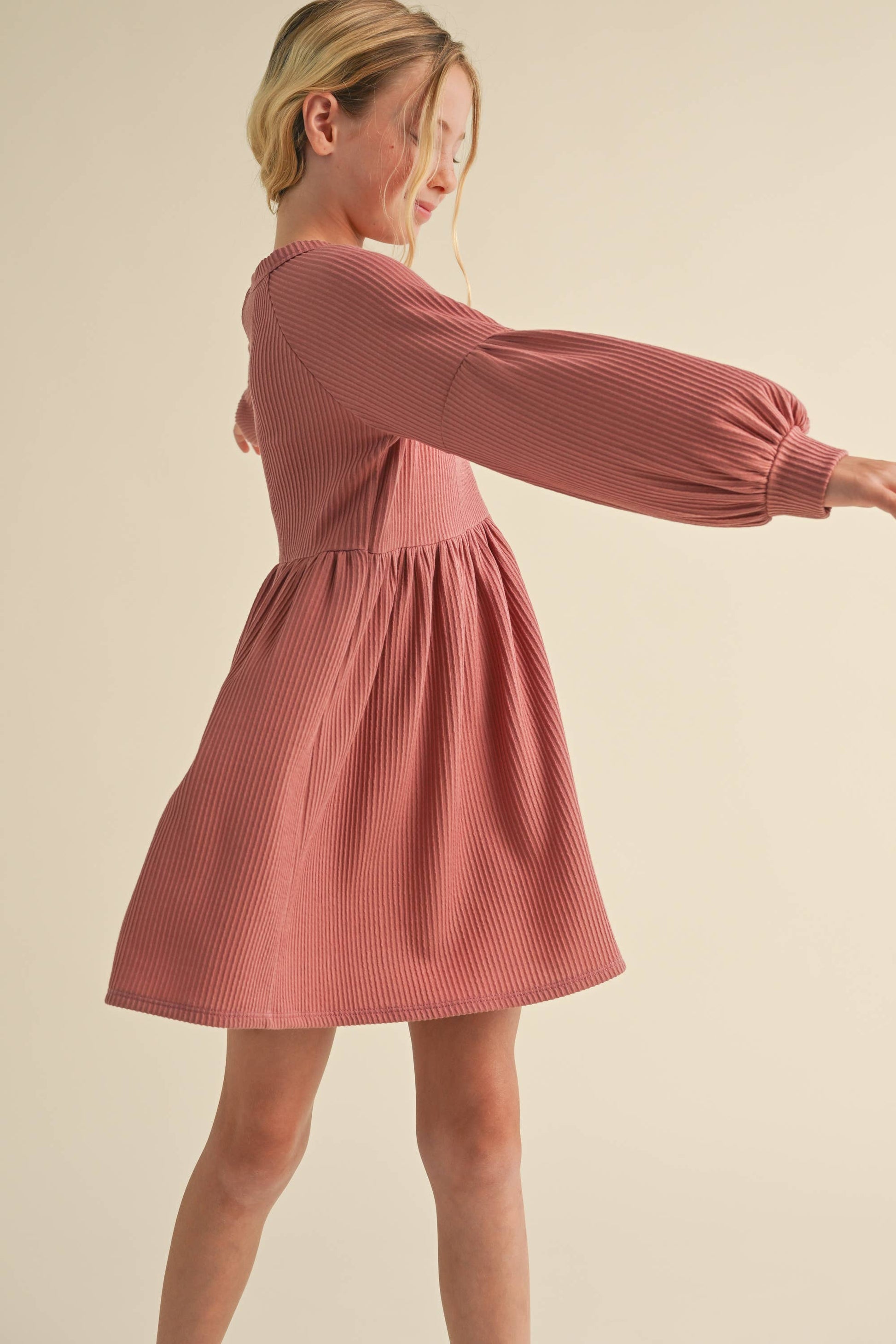 Woman wearing a pink ribbed dress against a beige background