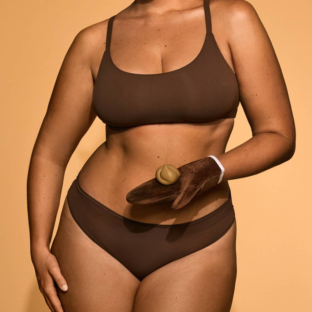 Person wearing a brown bikini holding a chocolate donut against a beige background