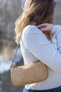 Person wearing a beige handbag over one shoulder with a blurred background
