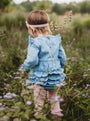 Child in a blue dress standing in a field with wildflowers