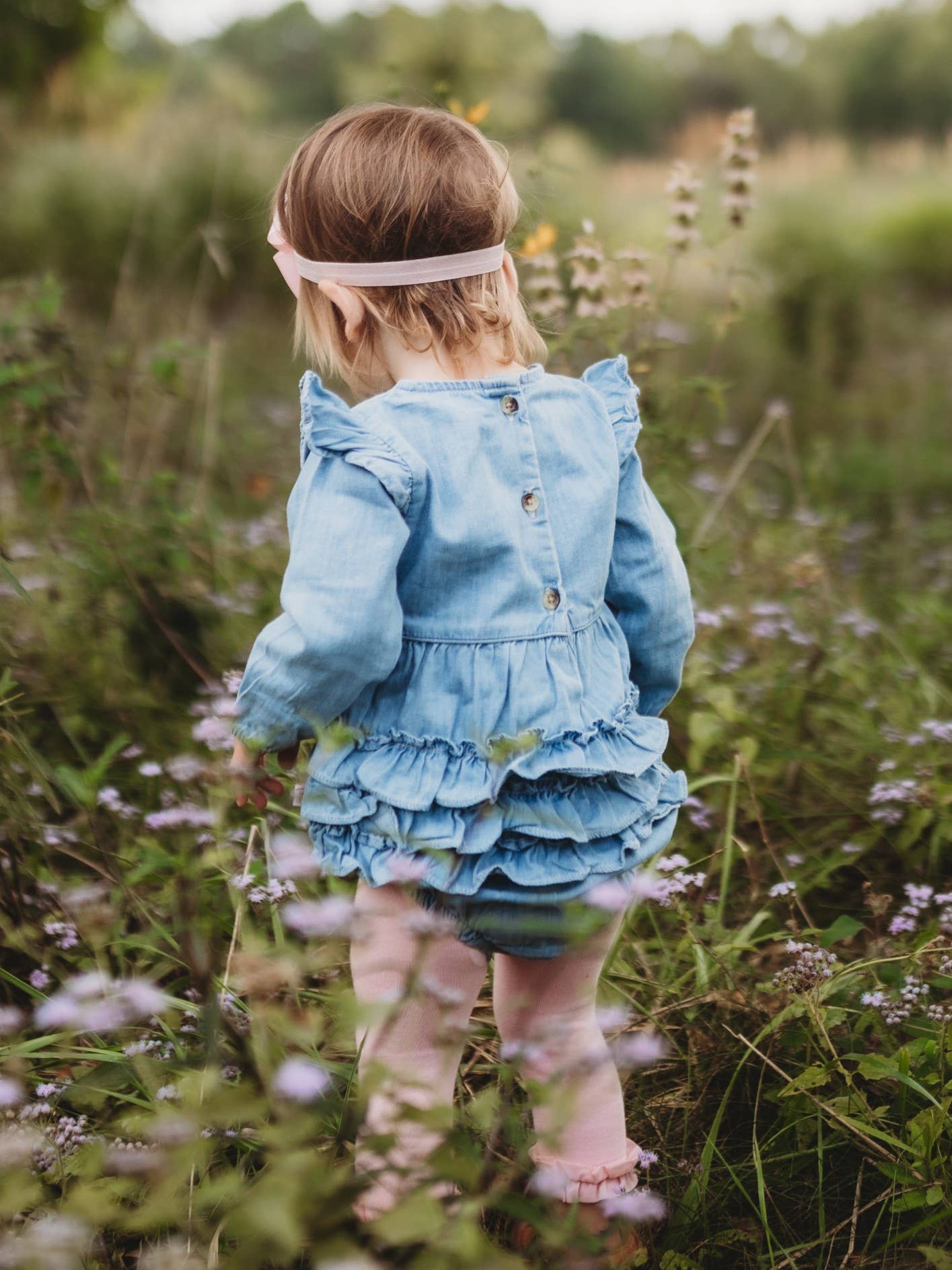 Child in a blue dress standing in a field with wildflowers