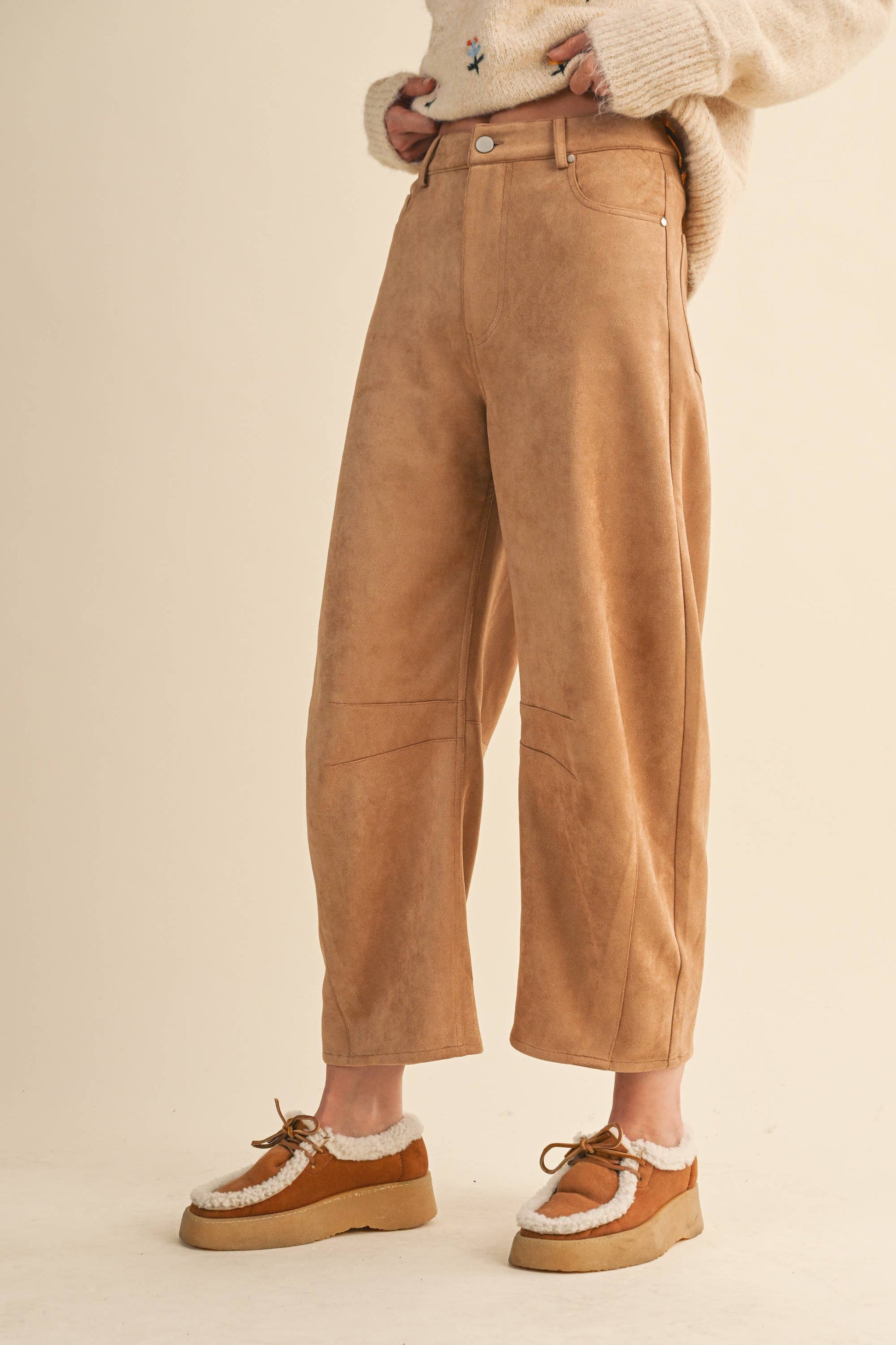 Person wearing tan corduroy pants with a cream sweater and brown shoes on a beige background