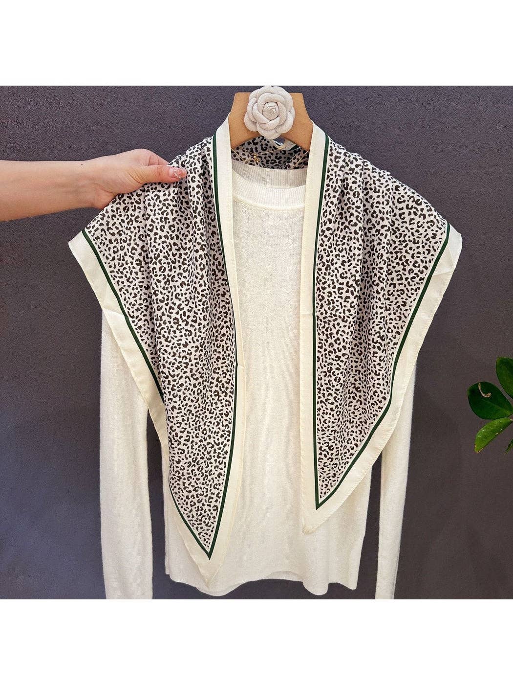 Leopard print triangle bandana with green-edged cream frame, neatly folded on hanger
