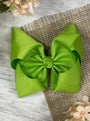 Two green hair bows on a textured surface with flowers around.